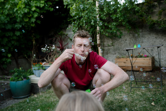 Father blowing bubbles for his daughter in their garden