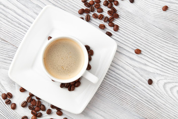 cup of coffee with coffee's beans over white wooden background, top view