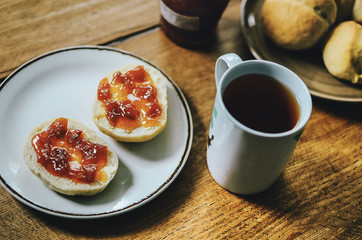 Cup of black tea with red jam on bread buns for tasty breakfast. Simple and delicious breakfast idea. Wooden table background.