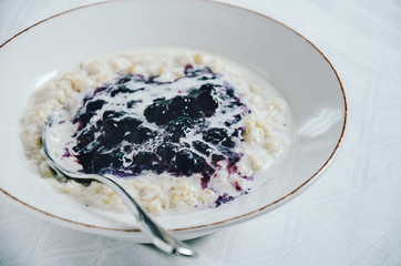 Homemade creamy porridge in a plate topped with blueberry sauce. Healthy start of the day, simple breakfast, warm meal for cold days.