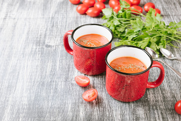 Two red mugs of homemade tomato soup with cream and parsley on wooden table. Copy spase for your text
