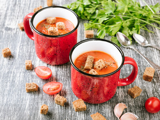 Red mug of homemade tomato cream soup with crackers or crouton and parsley on wooden table. Copy spase for your text