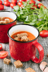 Red mug of homemade tomato cream soup with crackers or crouton and parsley on wooden table. Copy spase for your text
