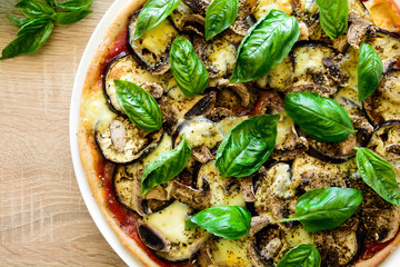 Vegetarian pizza with eggplant, tomato, mushrooms and basil on wooden background. Top view.