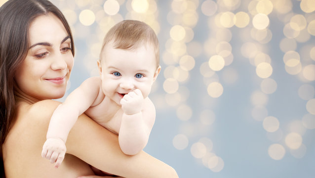 family and motherhood concept - happy smiling young mother with little baby over festive lights background