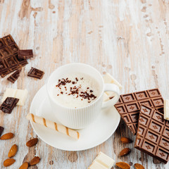 Cup of hot cocoa or Cappuccino or latte coffee with chocolate bar, almonds and whipped cream on wooden table