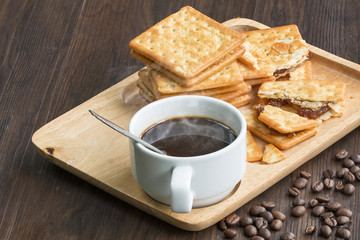 Black coffee,cracker and coffee bean on wood with warm morning light.Copy space.
