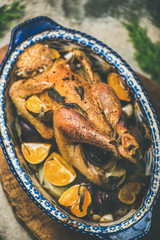 Roasted chicken with orange for Christmas eve celebration table and fir tree branches on wooden board over grey background, selective focus