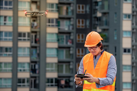Young Asian engineer man flying drone over construction site. Using unmanned aerial vehicle (UAV) for land and building site survey in civil engineering project.