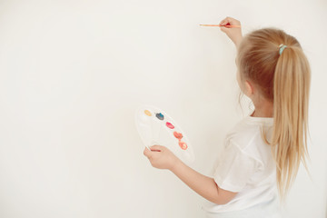 View from behind of a little girl painting on blank white wall.