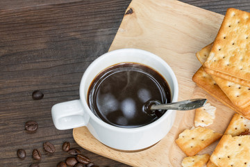 Black coffee,cracker and coffee bean on wood with warm morning light.Copy space.