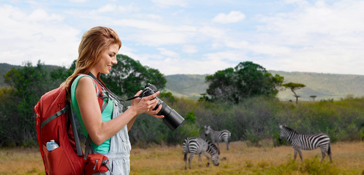 travel, tourism and photography concept - happy young woman with backpack and camera photographing over zebras in african savannah background
