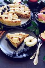 American tradition apple pie with apples, blueberry and cinnamon decorated apple leaves on dark wooden background. Flat lay. Still life. Toned