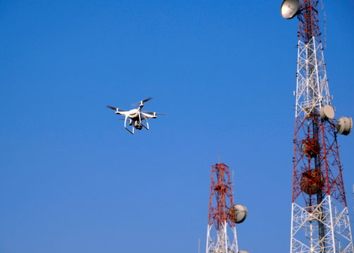 white drone flying in city near telecommunication tower