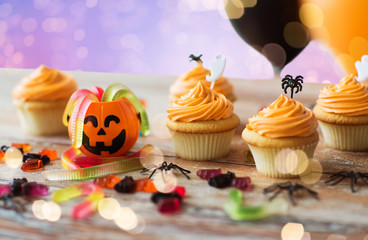 food, baking and holidays concept - cupcakes or muffins and candies with halloween party decorations on wooden table