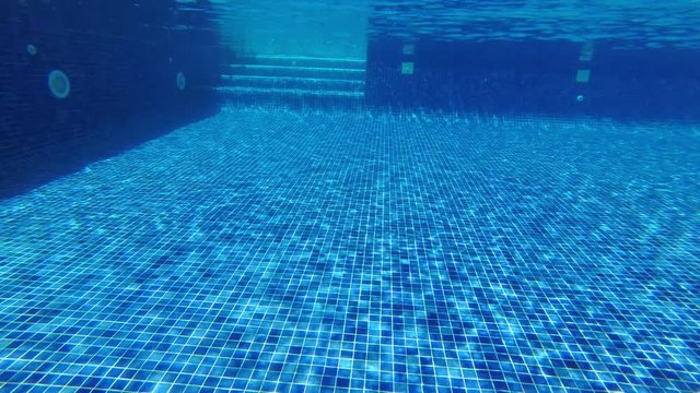 Underwater shoot of wide blue tiled swimming pool with shiny sunlight reflection