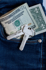 Keys to the house on a keychain and cash are lying in a pocket of blue jeans.