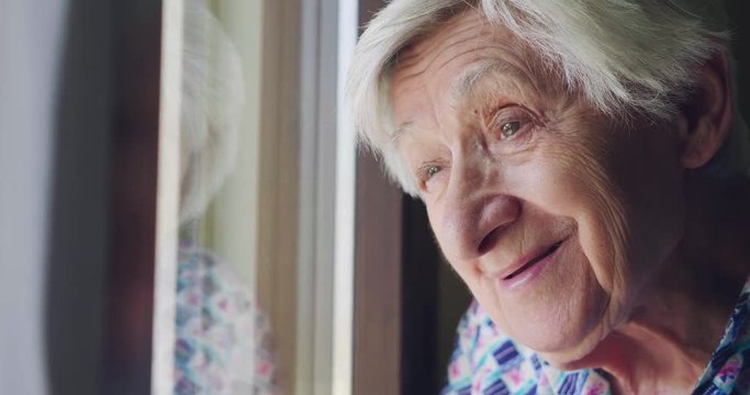 An old lady looks out the window and smiles. In the window. Concept of: life, drought, elderly support and nursing home and happiness.
