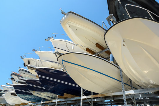 View from below of the hulls of motorboats racked one above another on two levels in a dry rack boat storage facility against blue sky.