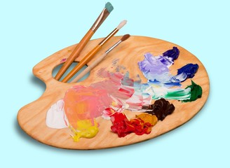 Wooden art palette with blobs of paint and a brushes on white