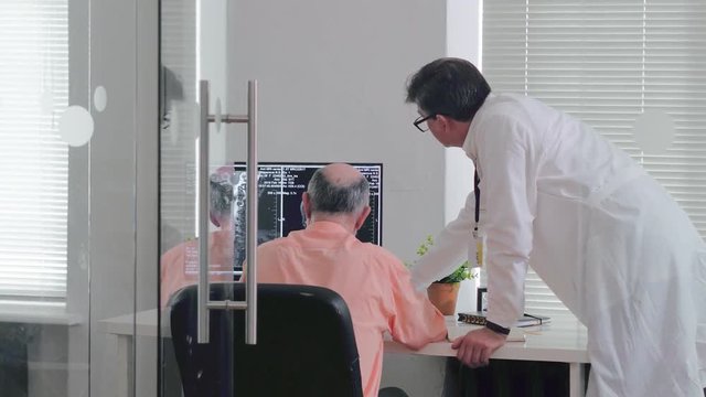 Two male oncologists working at computer in laboratory of scientific research cancer center. Doctors diagnose cancer on computer in oncology center
