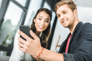 selective focus of multicultural smiling business colleagues using smartphone