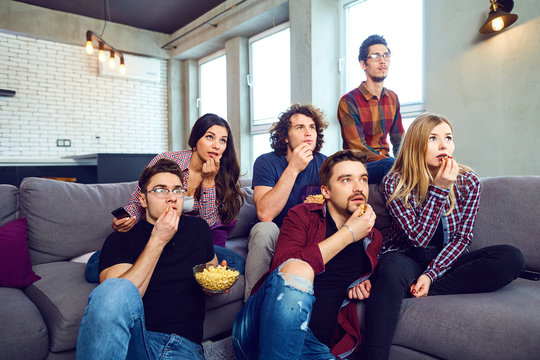 A group of friends eating pizza wathing tv sitting on the couch in the room.