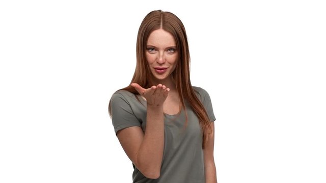Portrait of adorable ginger woman 20s playfully posing on camera giving air kiss with seductive look and smile, isolated over white background slow motion. Concept of emotions