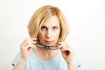 Closeup portrait of a woman takes off her glasses and looking directly into camera. Light background with copyspace.