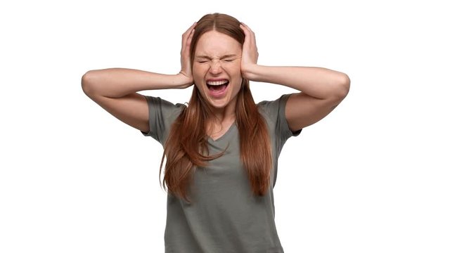 Portrait of shocked terrified woman 20s grabbing her head or covering ears and screaming in fear, isolated over white background slow motion. Concept of emotions