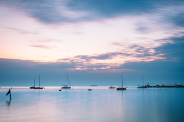 Fototapeta na wymiar Minimalist seascape with boats and big cargo ship in the distance after sunset at dusk after sunset