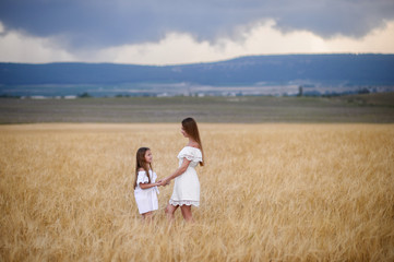 Beautiful family in a field of rye at sunset. A woman and child in amazing clothes walking through the field of rye.