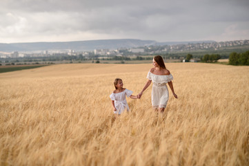 Beautiful family in a field of rye at sunset. A woman and child in amazing clothes walking through the field of rye.