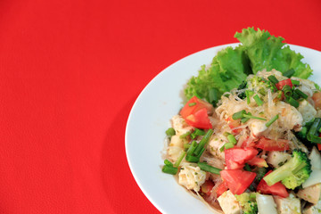Cellophane noodles salad with Vietnamese Pork Sausage and variety vegetable such as lettuce, tomato and onion in the round plate on the red floor. Crop subject and space.