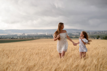 Beautiful family in a field of rye at sunset. A woman and child in amazing clothes walking through the field of rye.