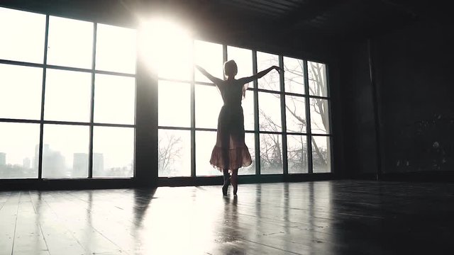 silhouette of a graceful ballerina who is spinning on tiptoes in the sun. Ballet dancer in pointe shoes and a long fluttering dress. slow motion
