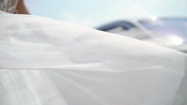 Bride and groom embracing in a city embankment, bride waving veil slowmotion at sunny day