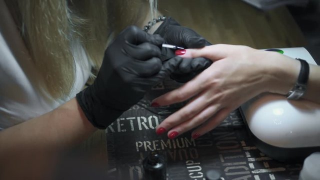 Professional nail artist is painting woman's nails with fixer nail polish in nail salon. Magazine pages flipping in the foreground and out of focus. Manicure treatment