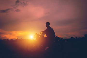 Silhouette of biker man  with his motorbike,he shoulder backpack. beside the natural lake and beautiful, enjoying freedom and active lifestyle, having fun on a bikers tour.sunset background and sky.