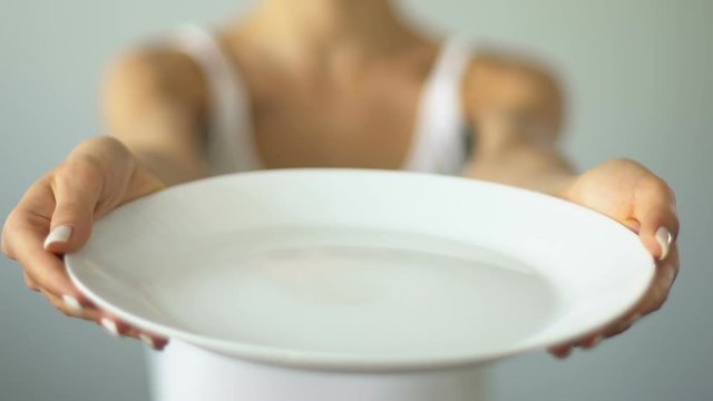 Diet concept, girl with taped mouth holding empty plate, malnutrition, anorexia