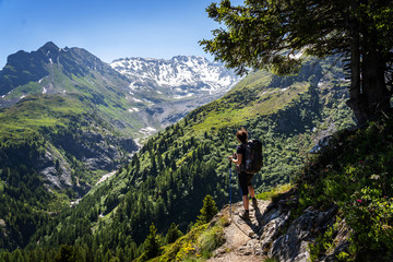 Fototapeta na wymiar Female traveler with backpack hiking mountain trail and admiring views of Swiss Alps in Val de Bagnes area, Switzerland.