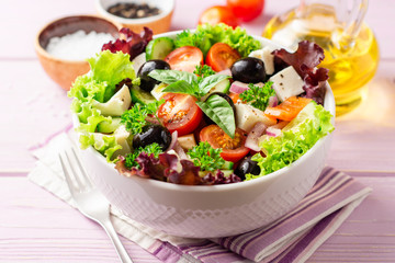 Fresh Greek salad with vegetables, feta cheese and black olives in white bowl on purple wooden...