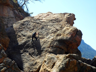 Hombre joven excursionista trepando en escalada libre rocas marrones y grises en día soleado de primavera en playa de Sa Foradada, Deià, Serra de Tramuntana, en isla de Mallorca, Islas Baleares.