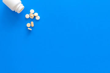 Medicine. Pills falling out of jar on blue background top view copy space