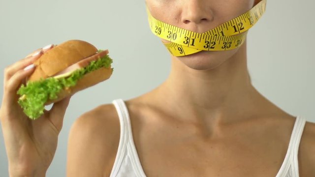 Female mouth wrapped with tape-line, girl wants burger but afraid of calories