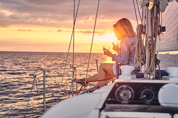 Female friends relaxing on the yacht with glasses of wine in the hands, during sunset on the high...
