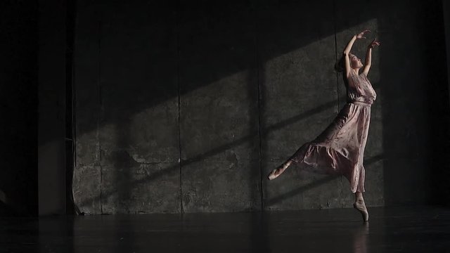 full of grace ballerina gracefully and beautifully dancing in pointe shoes and a long fluttering dress on a dark background in the studio. slow motion