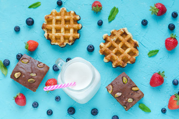 Waffles, brownie and smoothie on blue background with red berries. Flat lay.