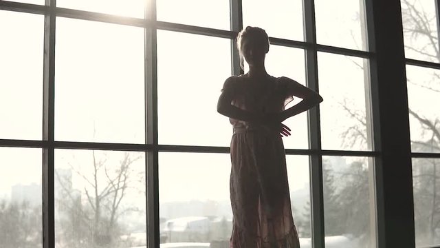 silhouette of a ballerina in the sunlight. A ballet dancer in a long fluttering dress is dancing against the background of a large window. slow motion