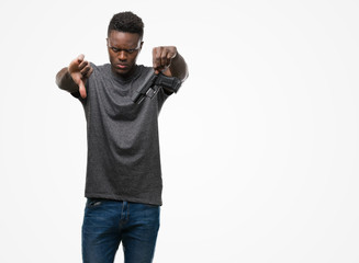 Fototapeta premium Young african american man holding a gun with angry face, negative sign showing dislike with thumbs down, rejection concept